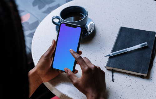 iPhone mockup on a table with cup of coffee and black notebook by the side