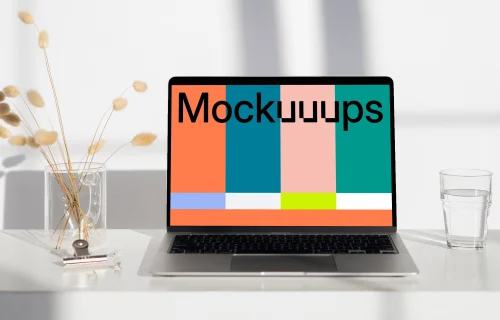 MacBook mockup on a white table with a glass of water at the side