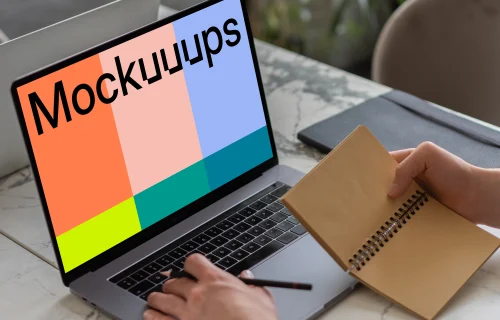 MacBook Pro mockup on a table with a jotter held beside it