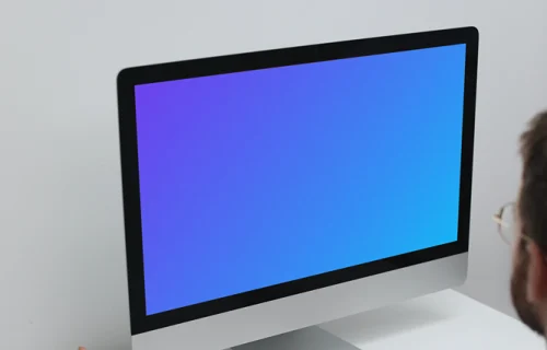 Man working on his iMac on a white table mockup