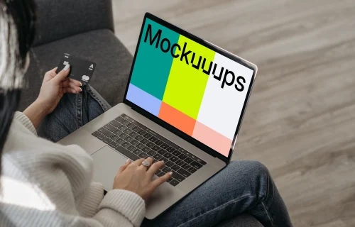Mockup of female user on a couch shopping online with her grey MacBook and a MasterCard in hand