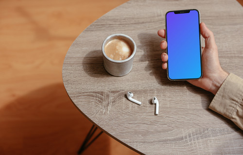 Simple handheld iPhone mockup held on the table with a pair of Airpods at the side