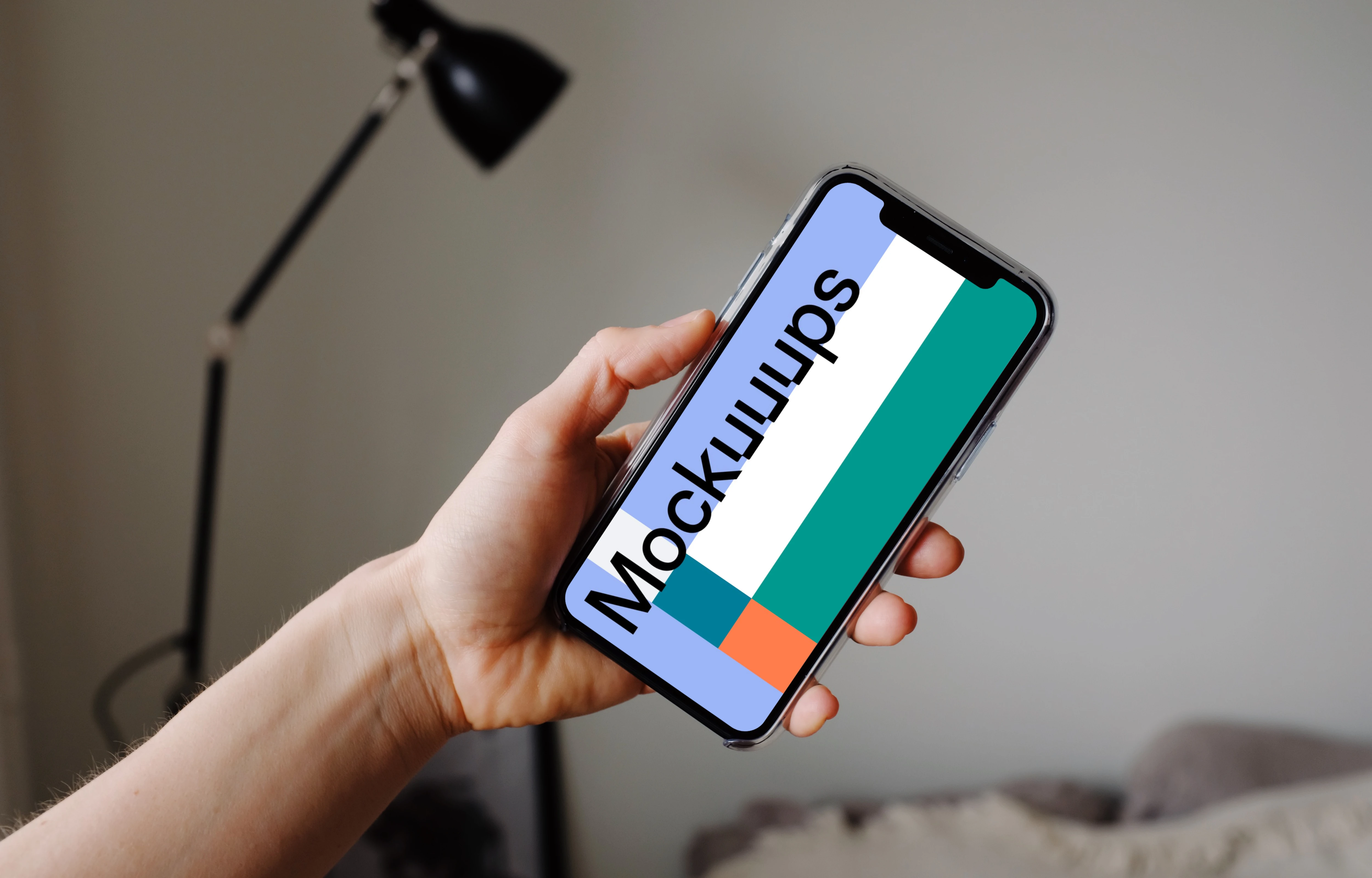 iPhone 12 Pro mockup held by user with a reading lamp in the background