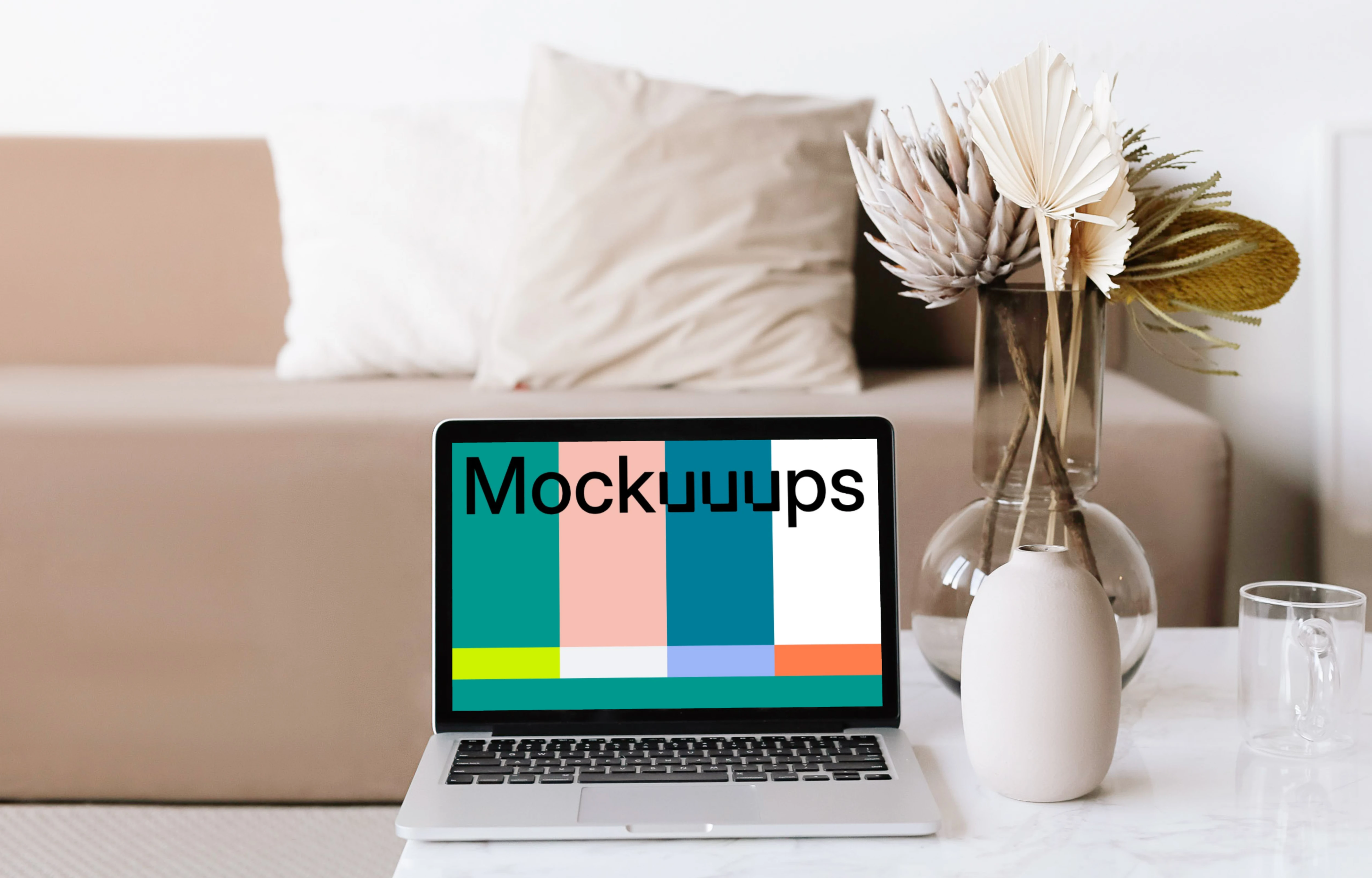 MacBook mockup on a white center table with glass cup and transparent flower po