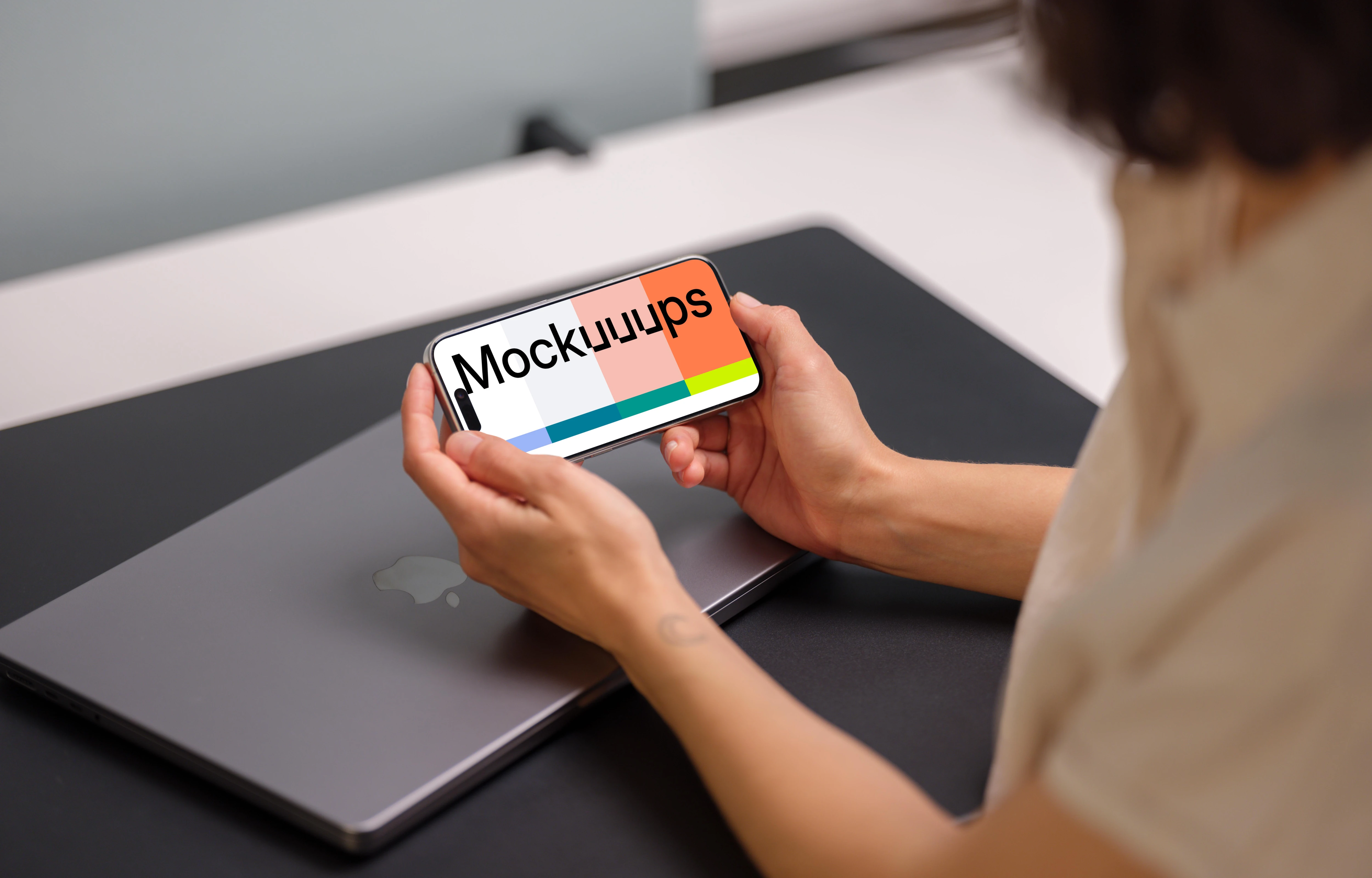 iPhone 15 Pro mockup in a woman's hand over a laptop