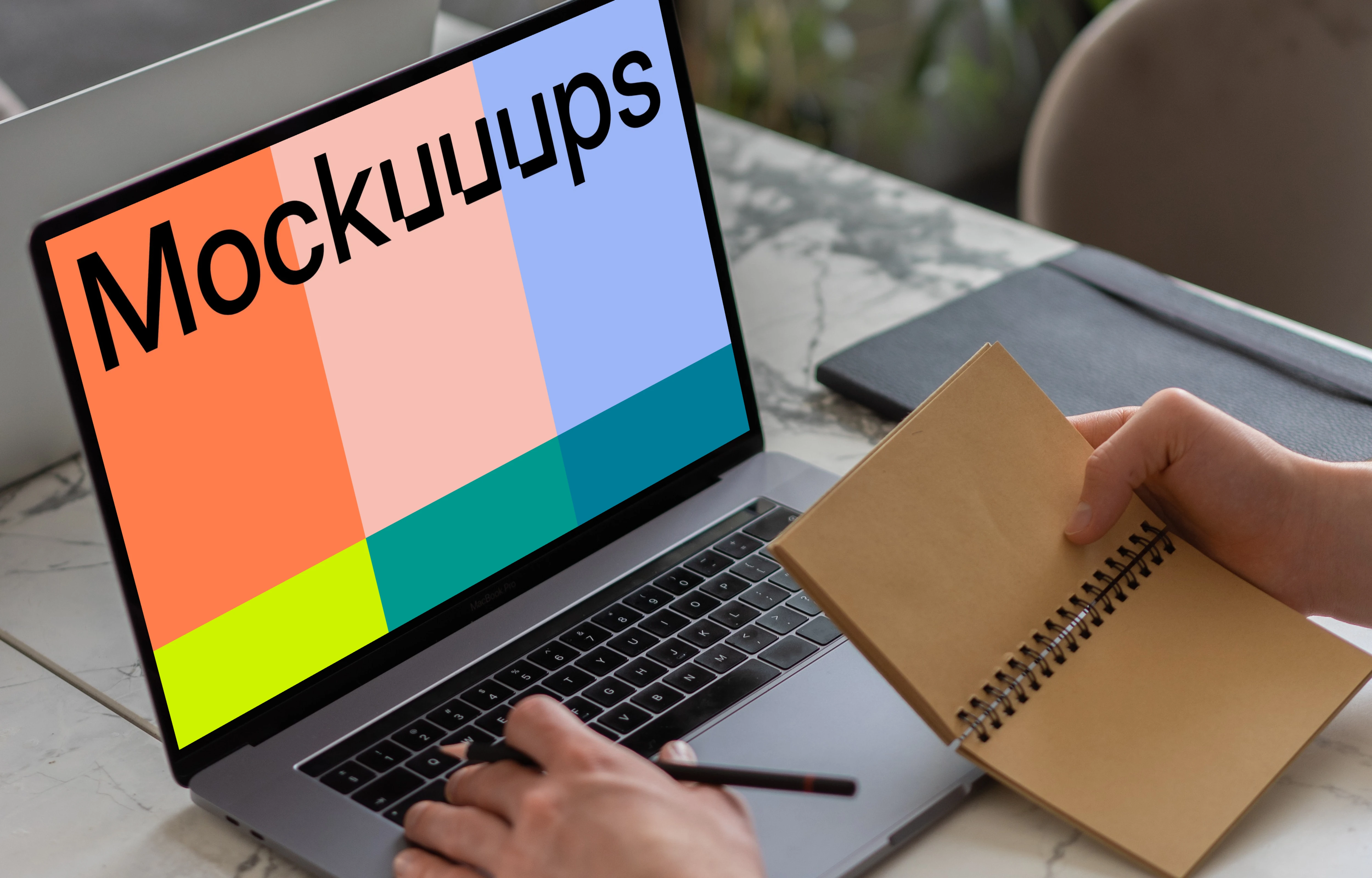 MacBook Pro mockup on a table with a jotter held beside it