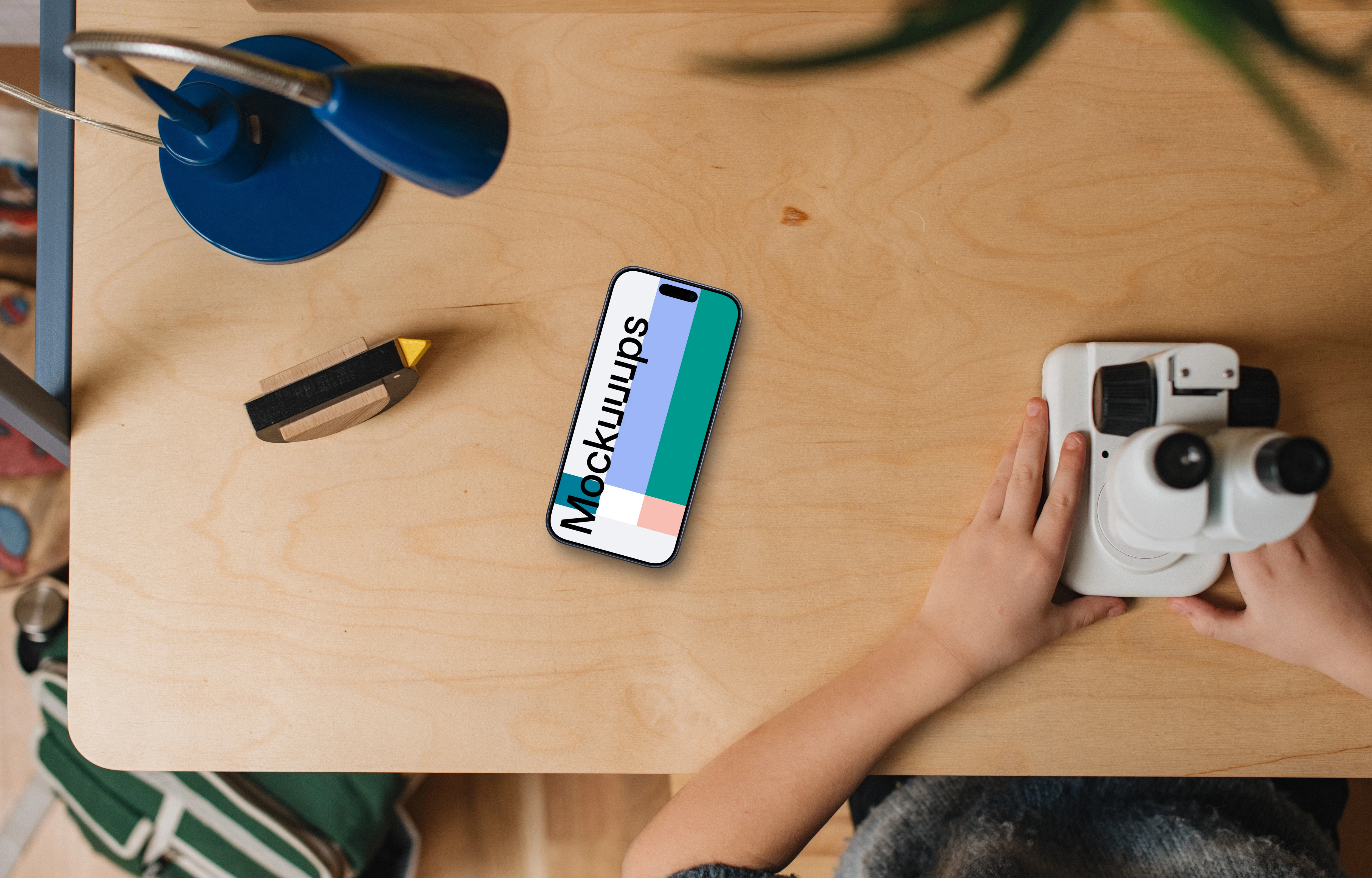 Smartphone mockup on wooden desk with kids' hands and toys