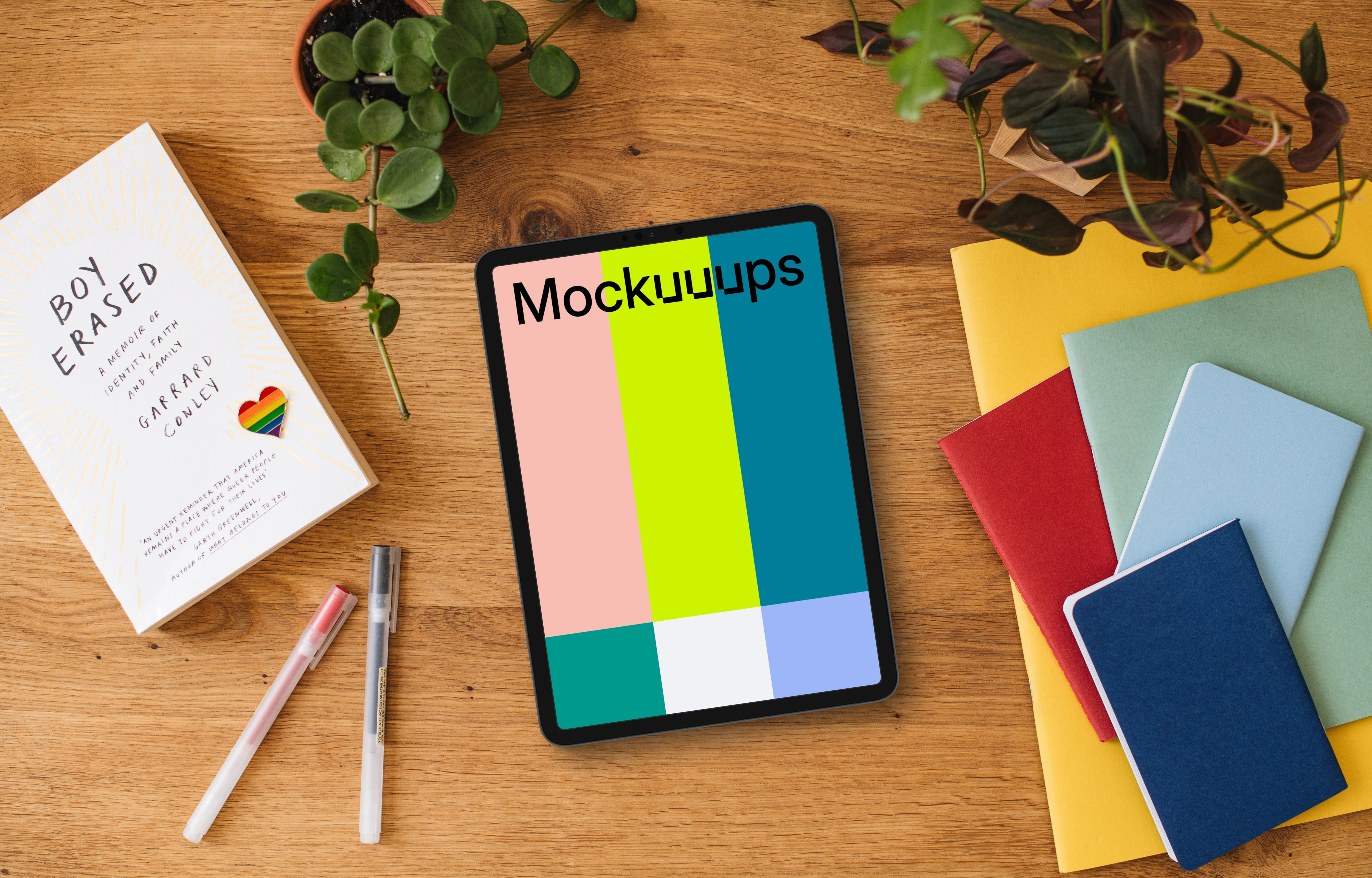 Tablet mockup on a wooden desk with pride enamel pin and colorful notebooks