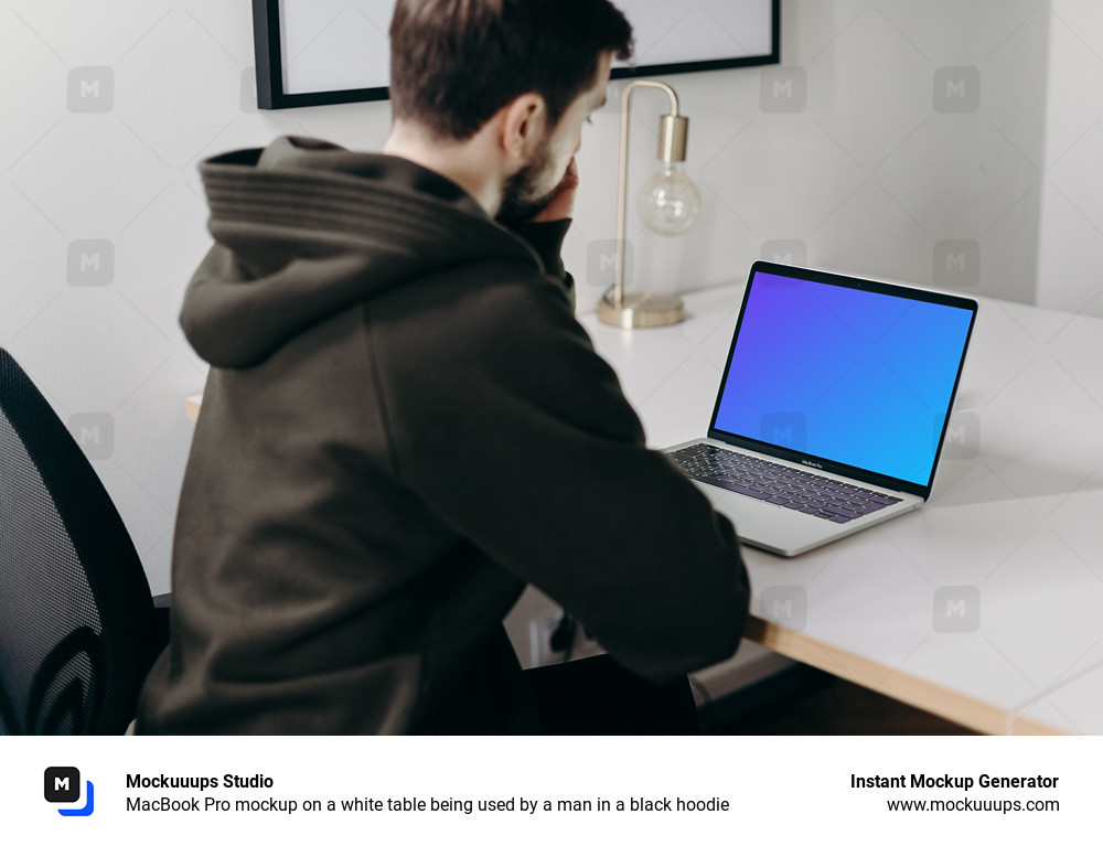 MacBook Pro mockup on a white table being used by a man in a black hoodie