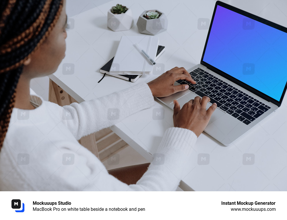 MacBook Pro on white table beside a notebook and pen