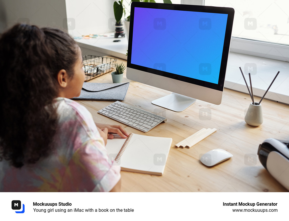 Young girl using an iMac with a book on the table