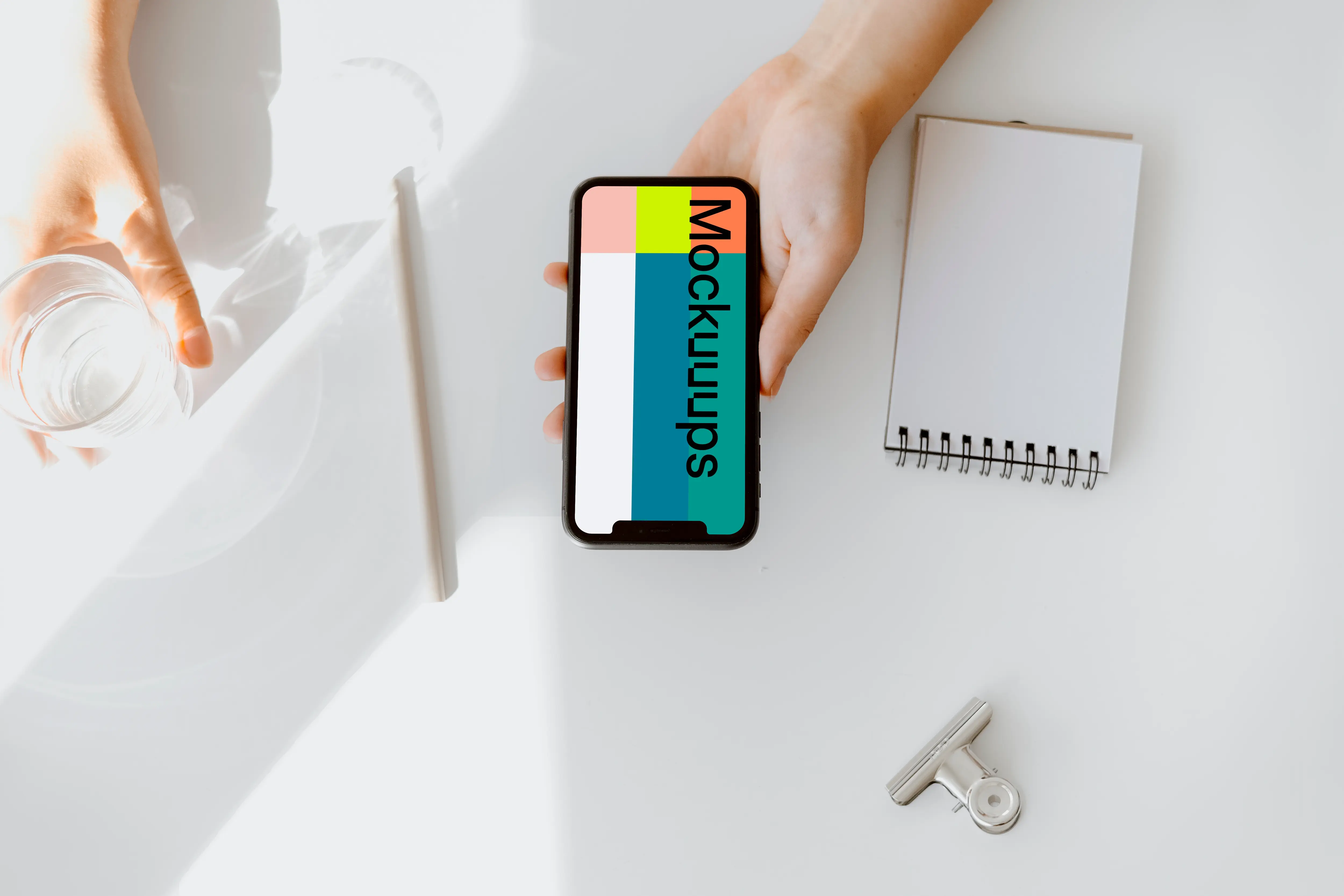 iPhone mockup held above a white table by a user with a glass of water at the side