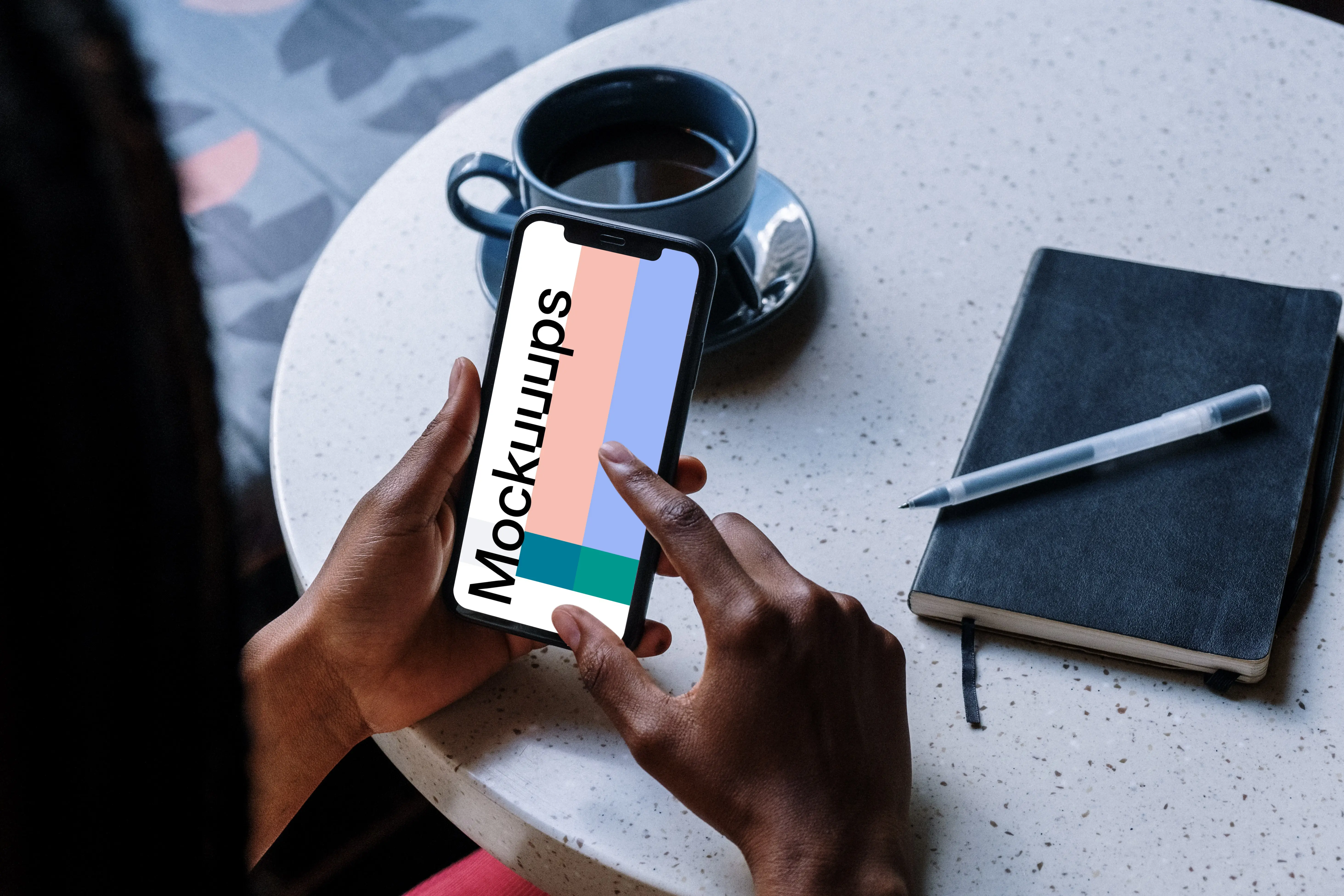 iPhone mockup on a table with cup of coffee and black notebook by the side