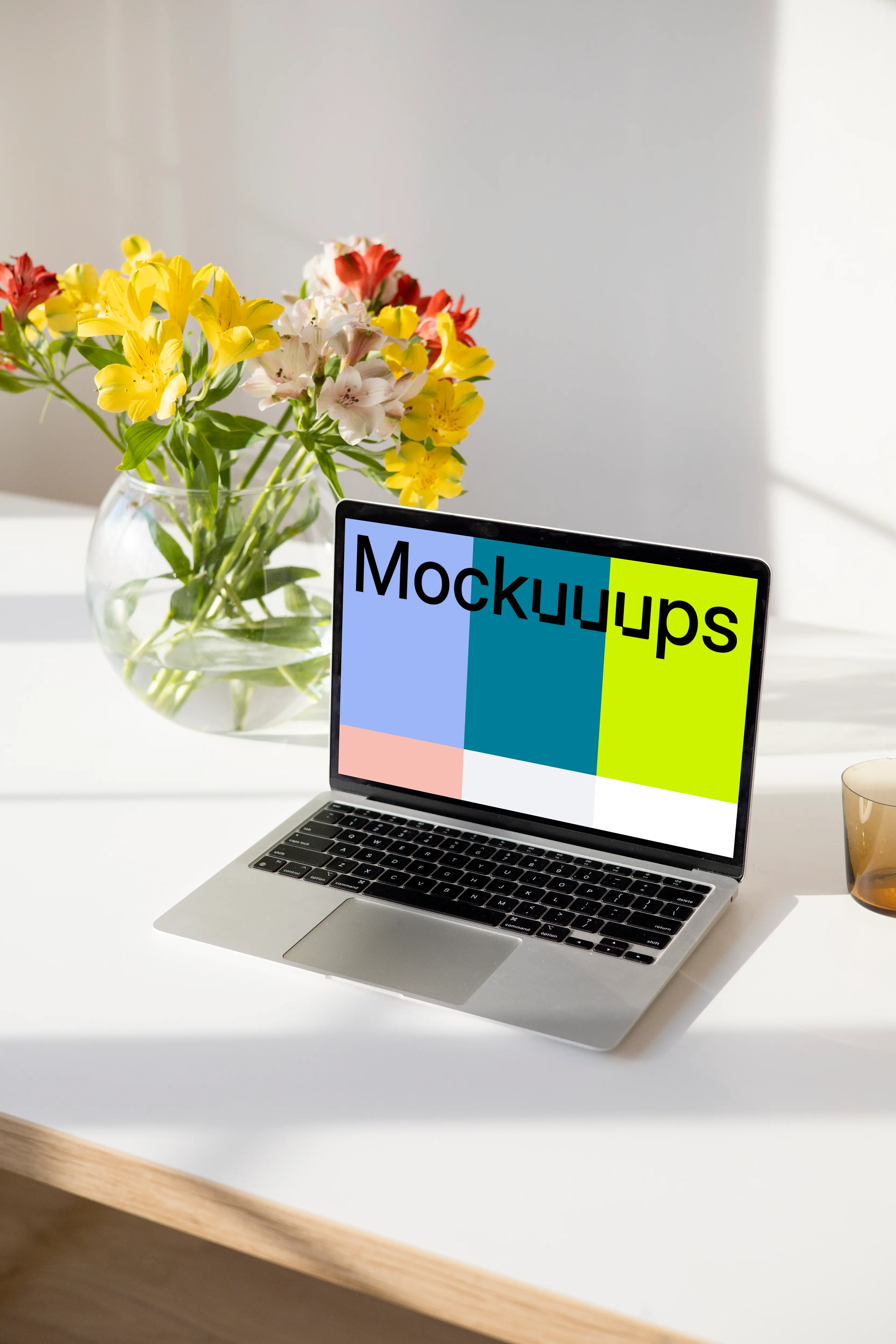 MacBook mockup on a white table beside a bowl-shaped flower vase close