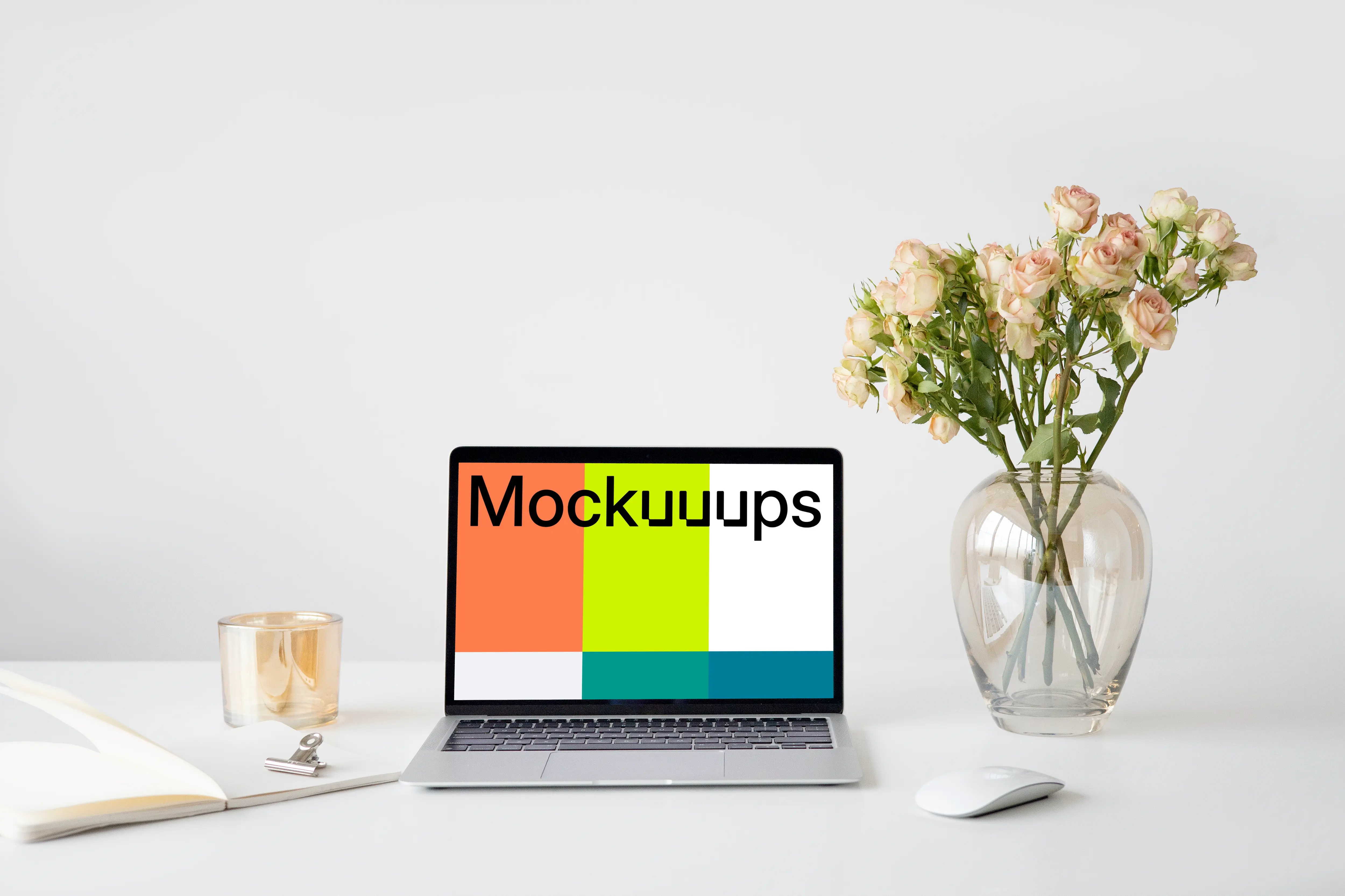MacBook mockup on a white table with a wireless mouse and a vase of rose