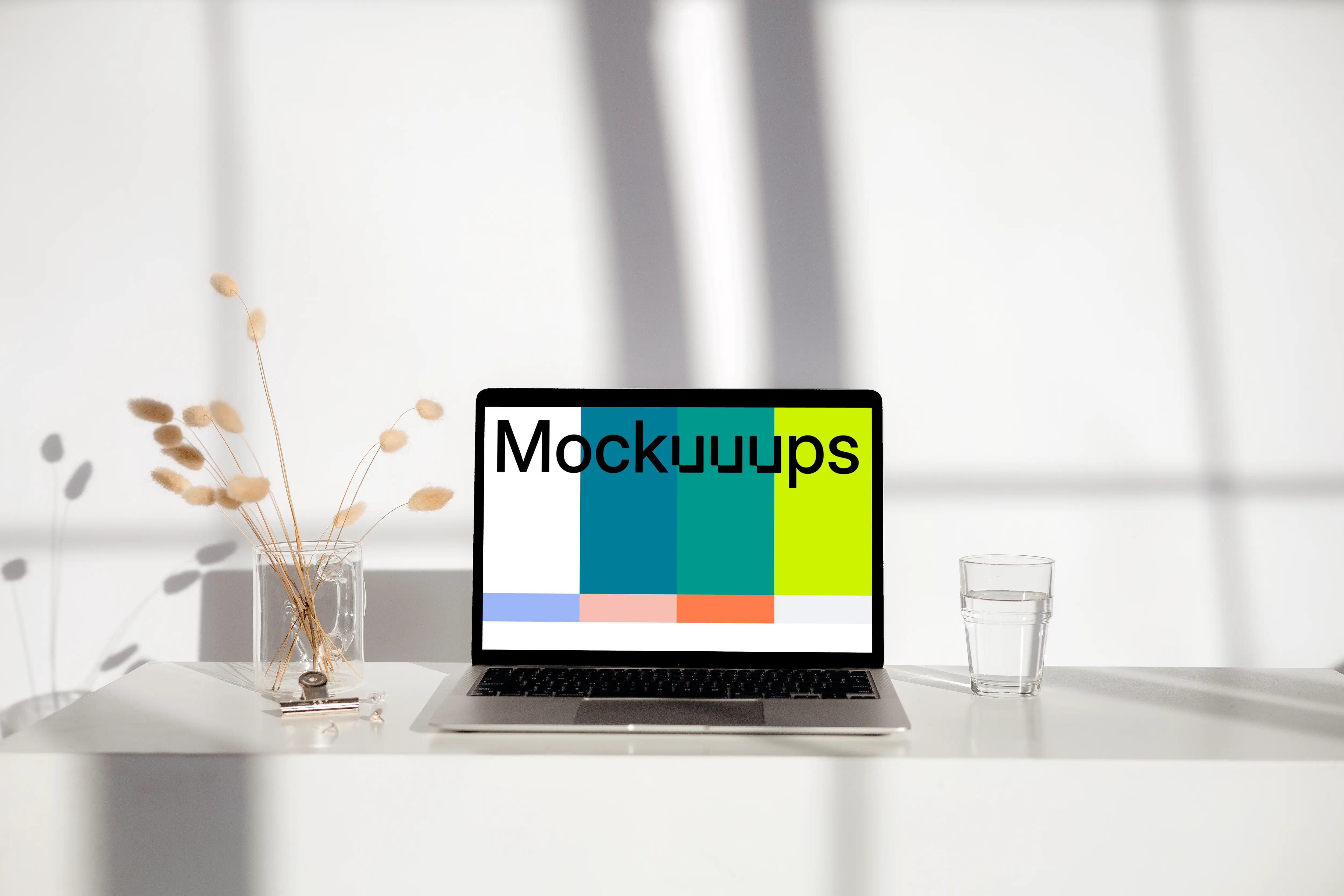 MacBook mockup on a white table with glass of water next to it