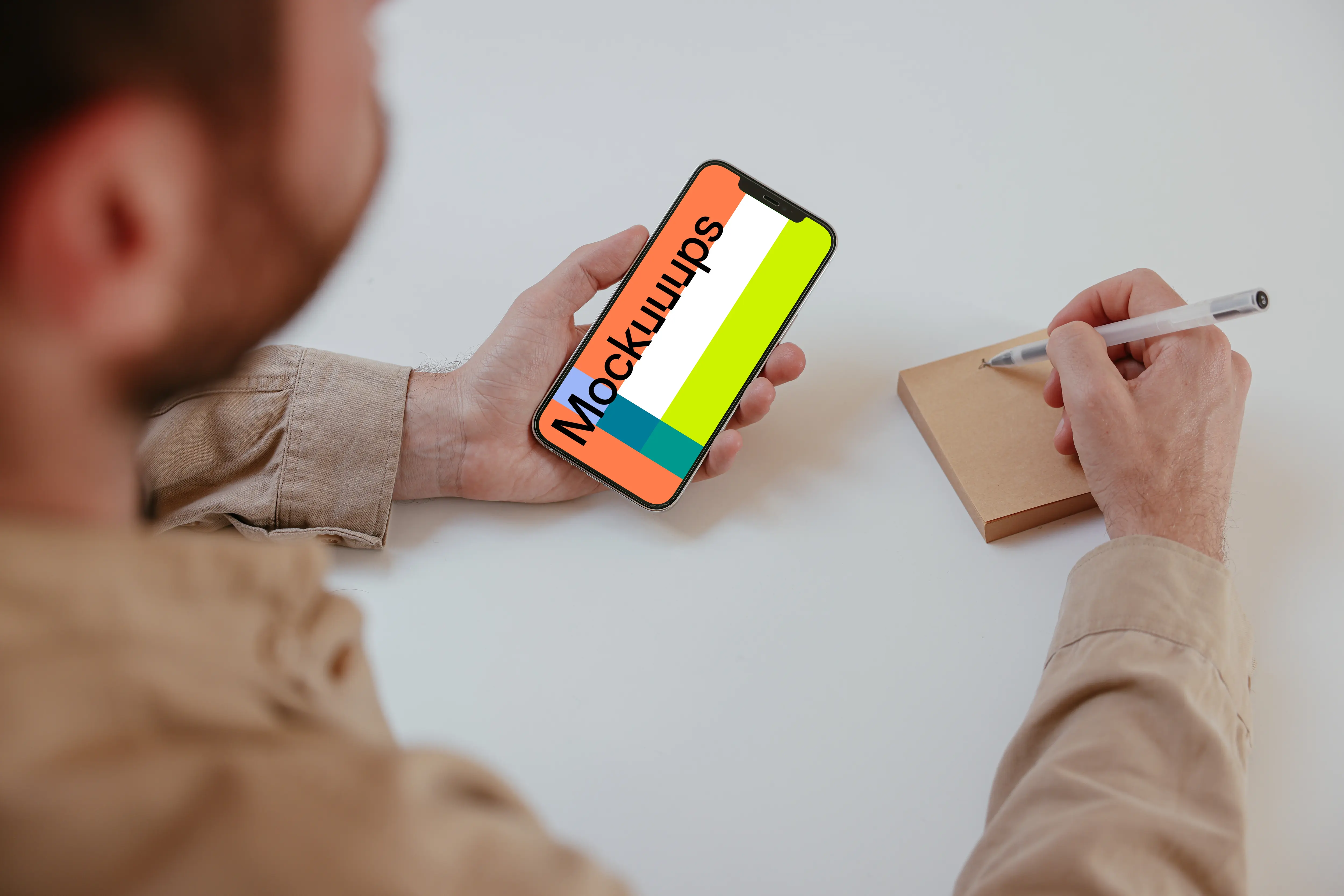 User holding an iPhone and writing into a sticky note mockup