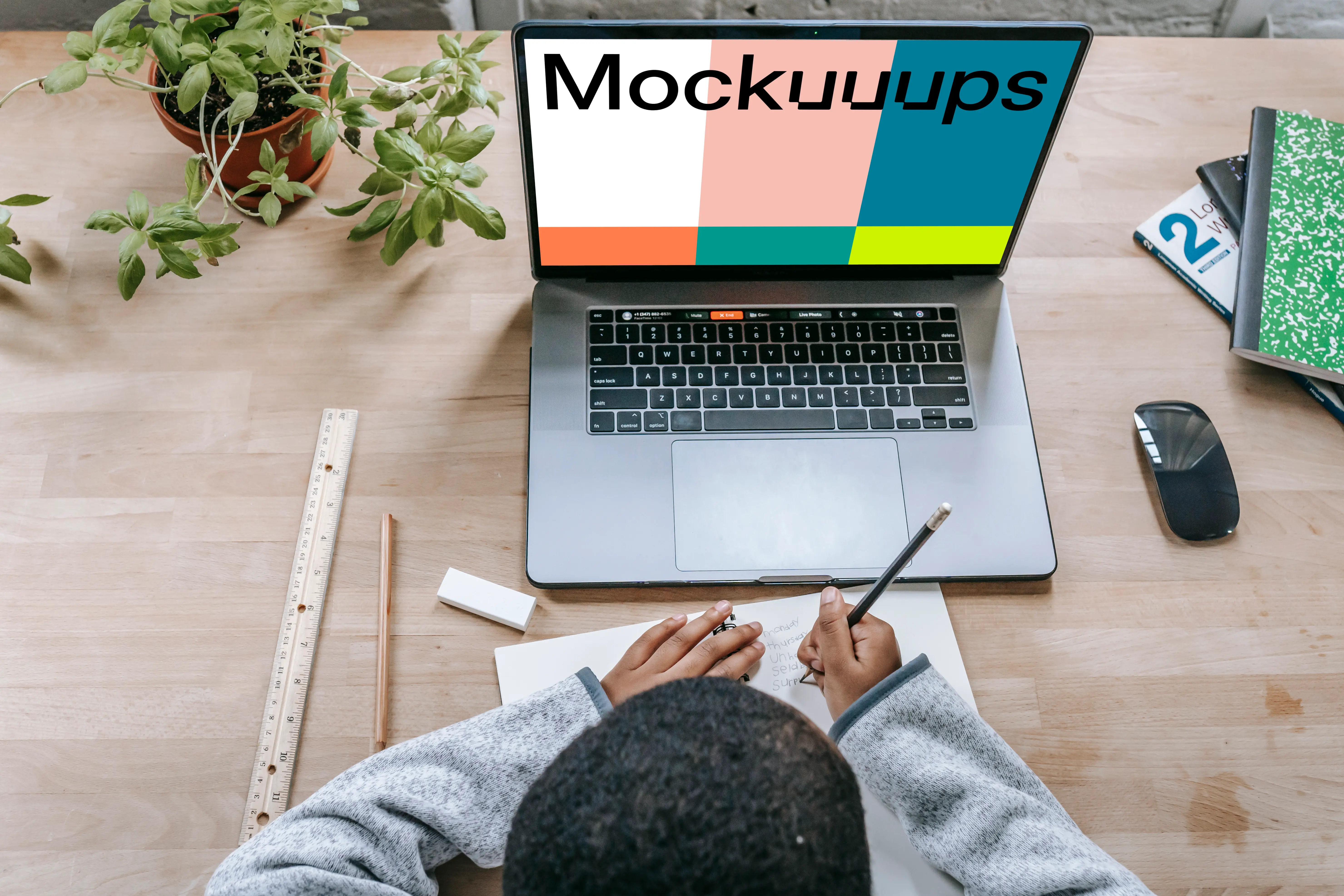 Young boy writing in a book with a MacBook Pro on the same table