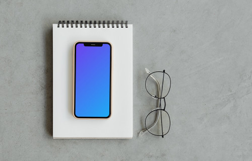 iPhone mockup on a jotter with reading glasses by the side.