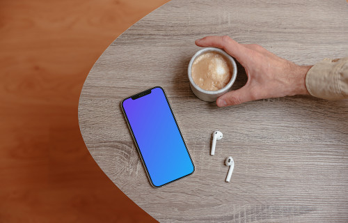 iPhone mockup on a wooden table next to a cup of coffee and a pair of AirPods.