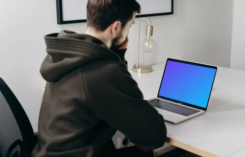 MacBook Pro mockup on a white table being used by a man in a black hoodie