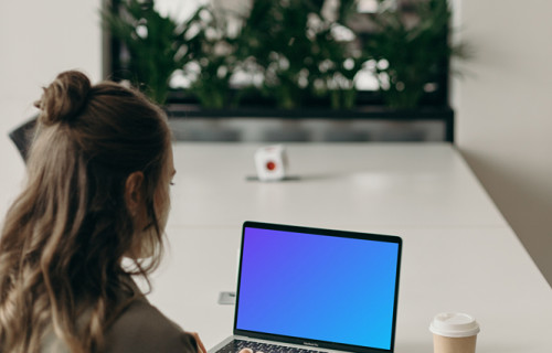 MacBook Pro mockup on a white table in use by a woman