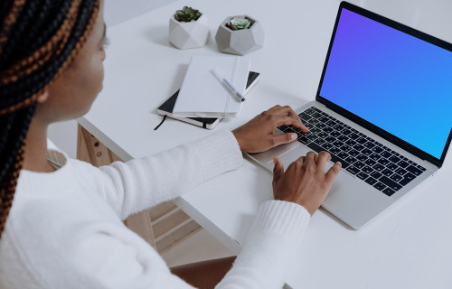 MacBook Pro on white table beside a notebook and pen