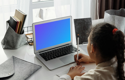 Mockup of Young girl viewing her MacBook Air screen and writing in a book