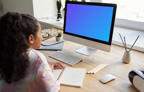 Young girl using an iMac with a book on the table