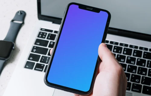 iPhone mockup held above a MacBook by a user in corporate dressing
