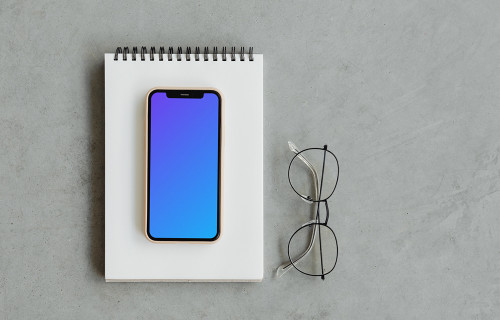 iPhone mockup on a jotter with reading glasses by the side.