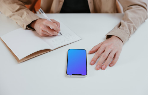 iPhone mockup on a white table next to a notebook