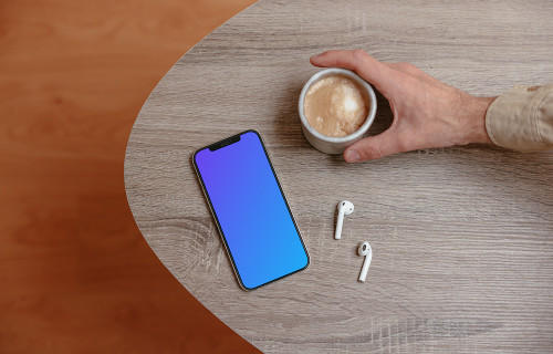 iPhone mockup on a wooden table next to a cup of coffee and a pair of AirPods.