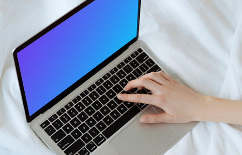 MacBook mockup on a white bed with a user typing on the laptop