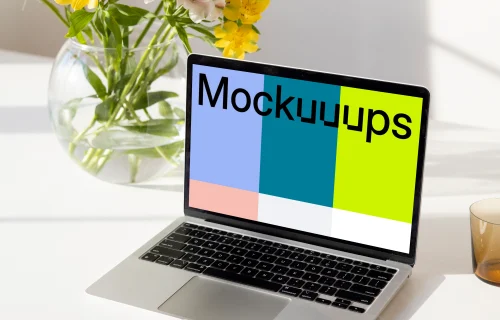 MacBook mockup on a white table beside a bowl-shaped flower vase close