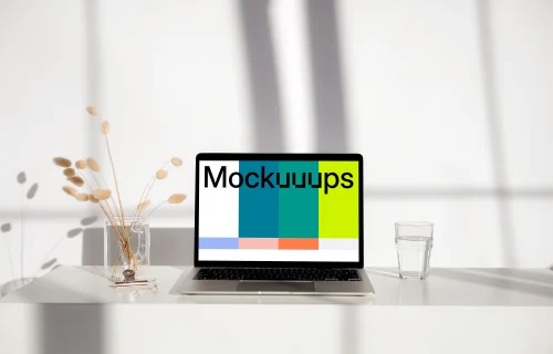 MacBook mockup on a white table with glass of water next to it