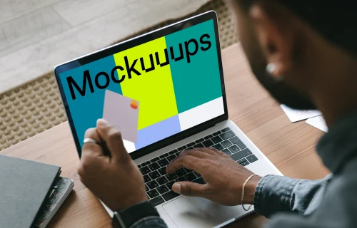 Man in grey shirt shopping mockup paying online with Mastercard on grey MacBook 