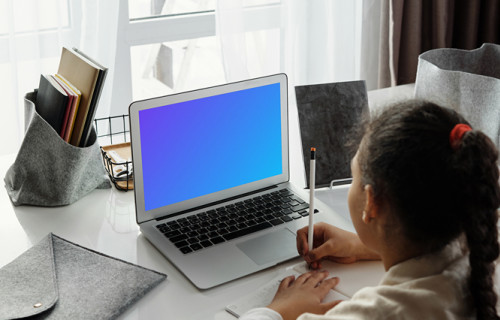 Mockup of Young girl viewing her MacBook Air screen and writing in a book