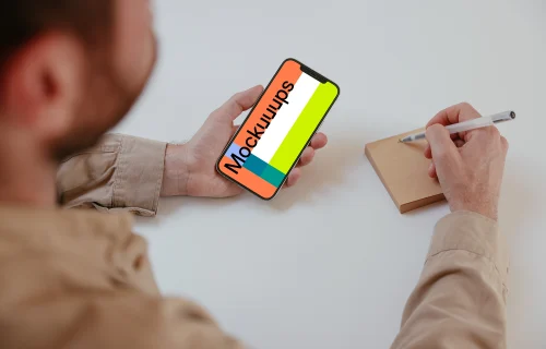 User holding an iPhone and writing into a sticky note mockup