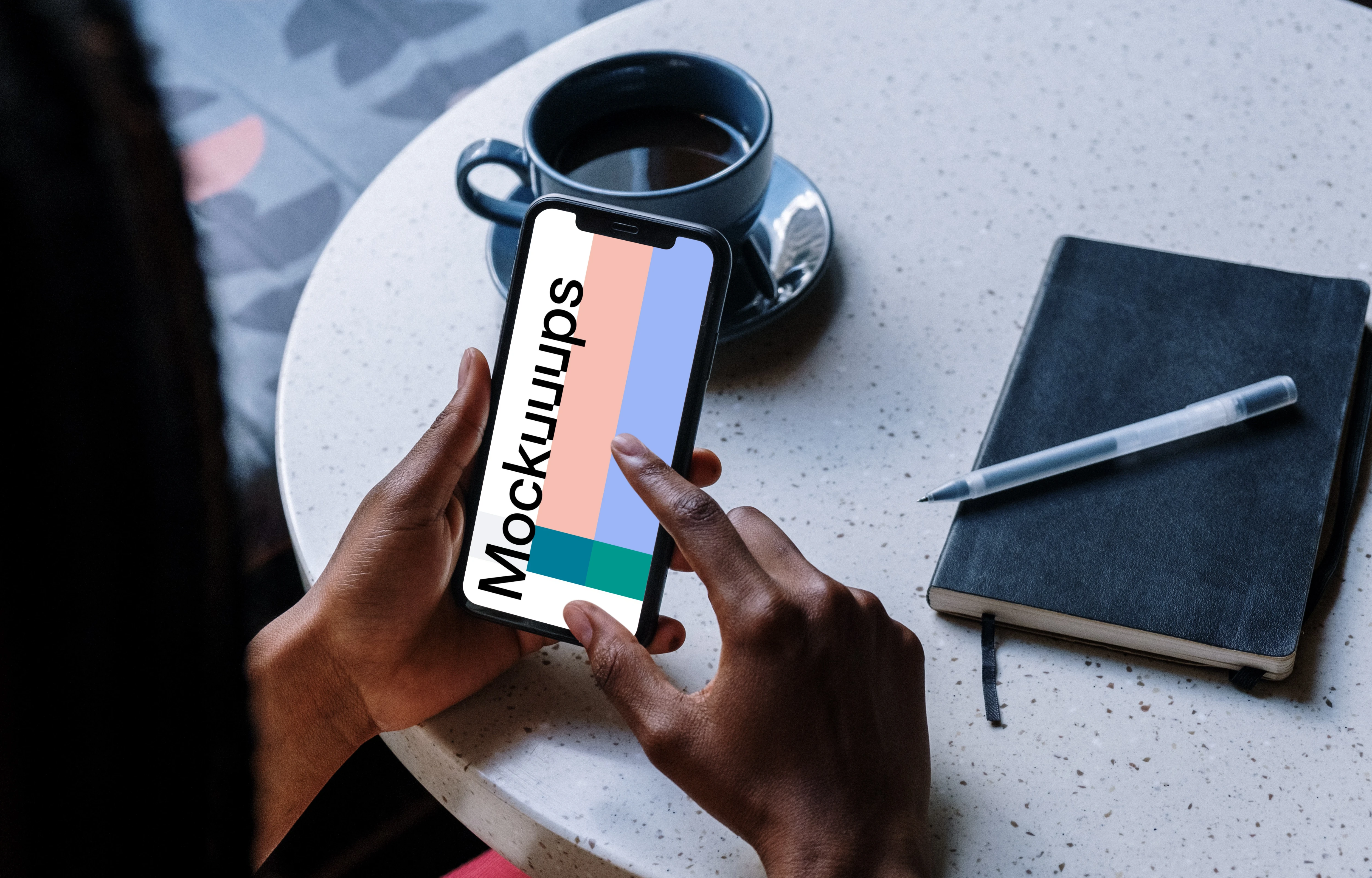 iPhone mockup on a table with cup of coffee and black notebook by the side