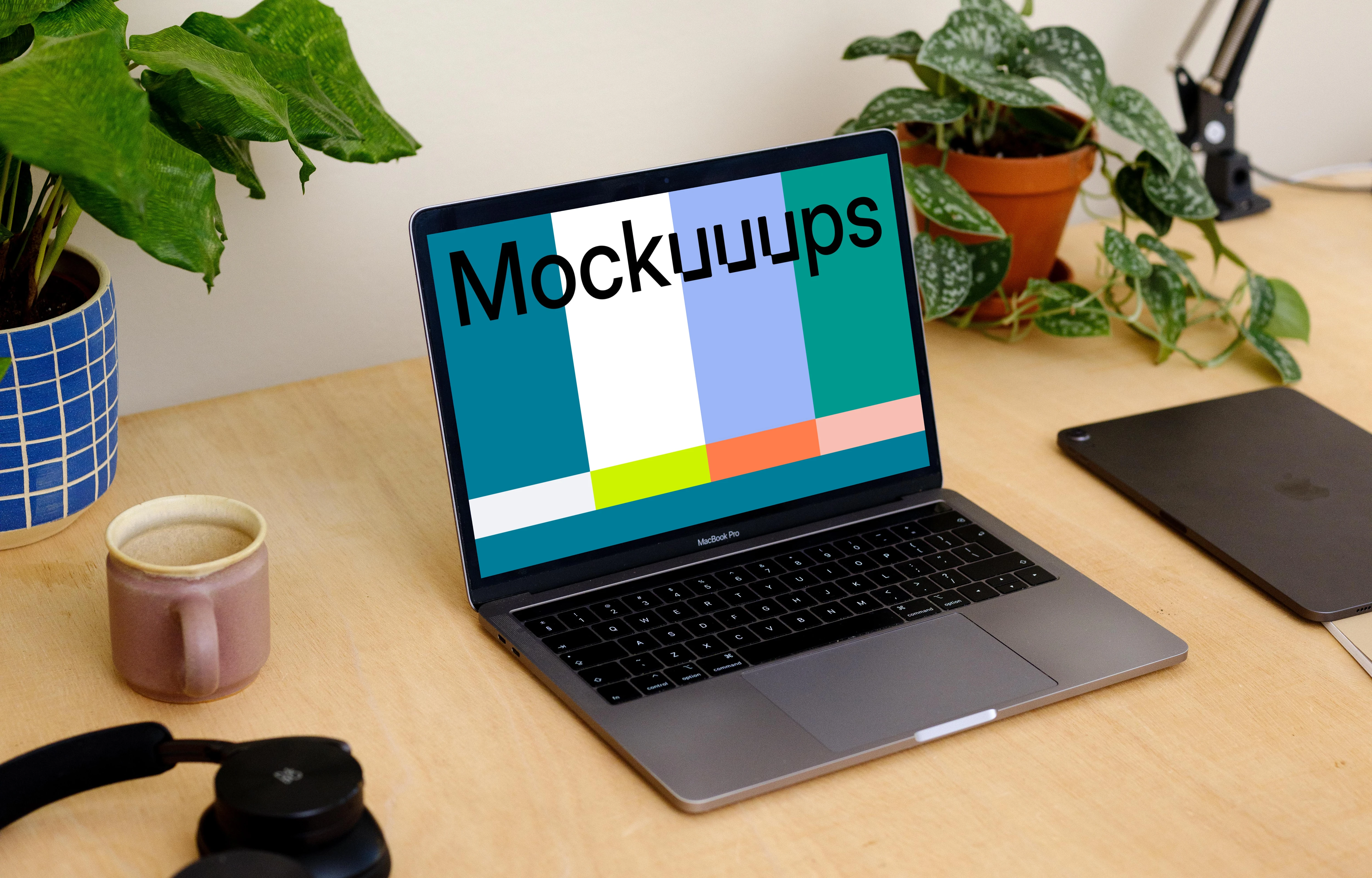 Grey MacBook Pro mockup with a coffee mug and an iPad at the side.