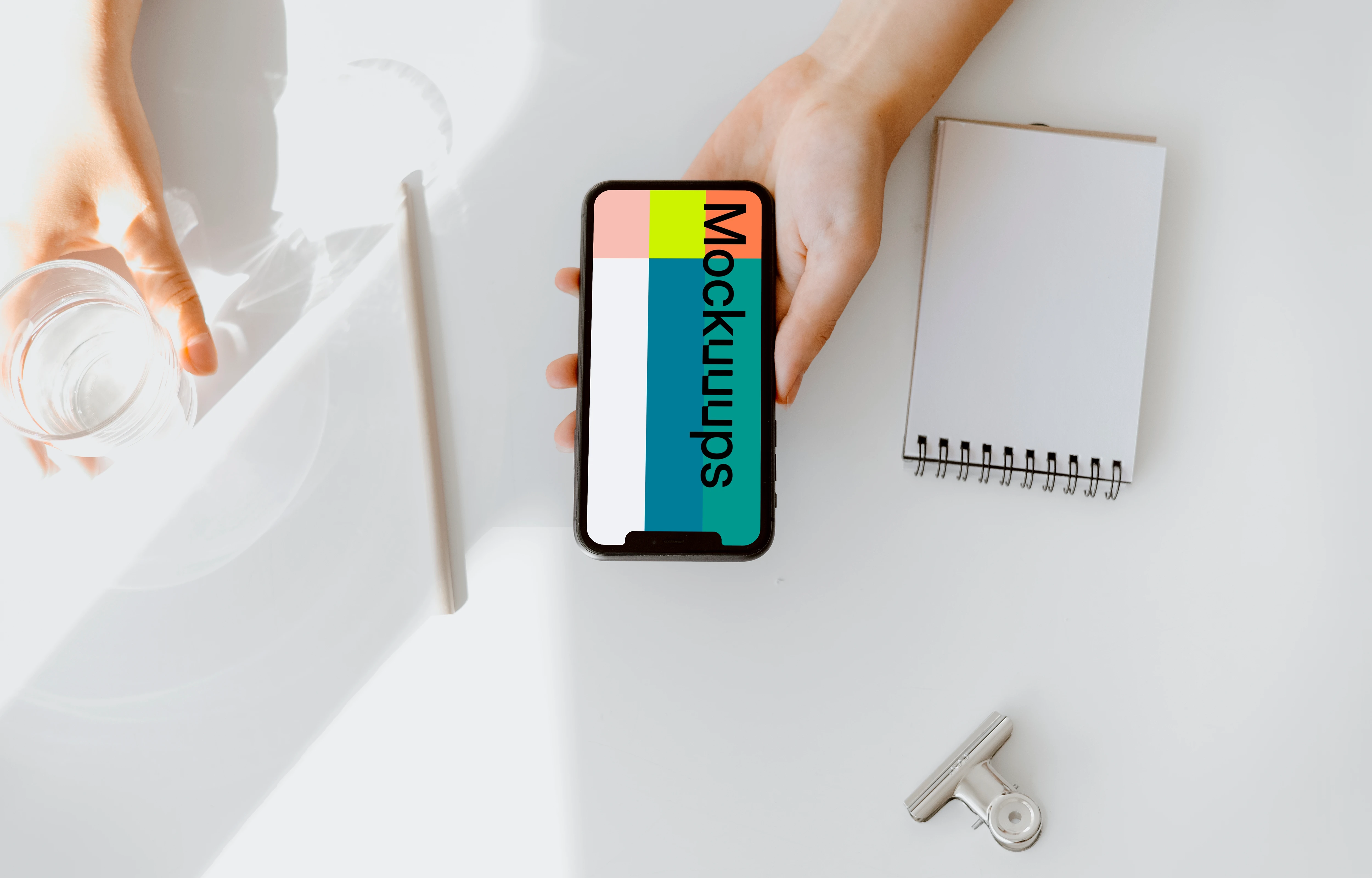 iPhone mockup held above a white table by a user with a glass of water at the side