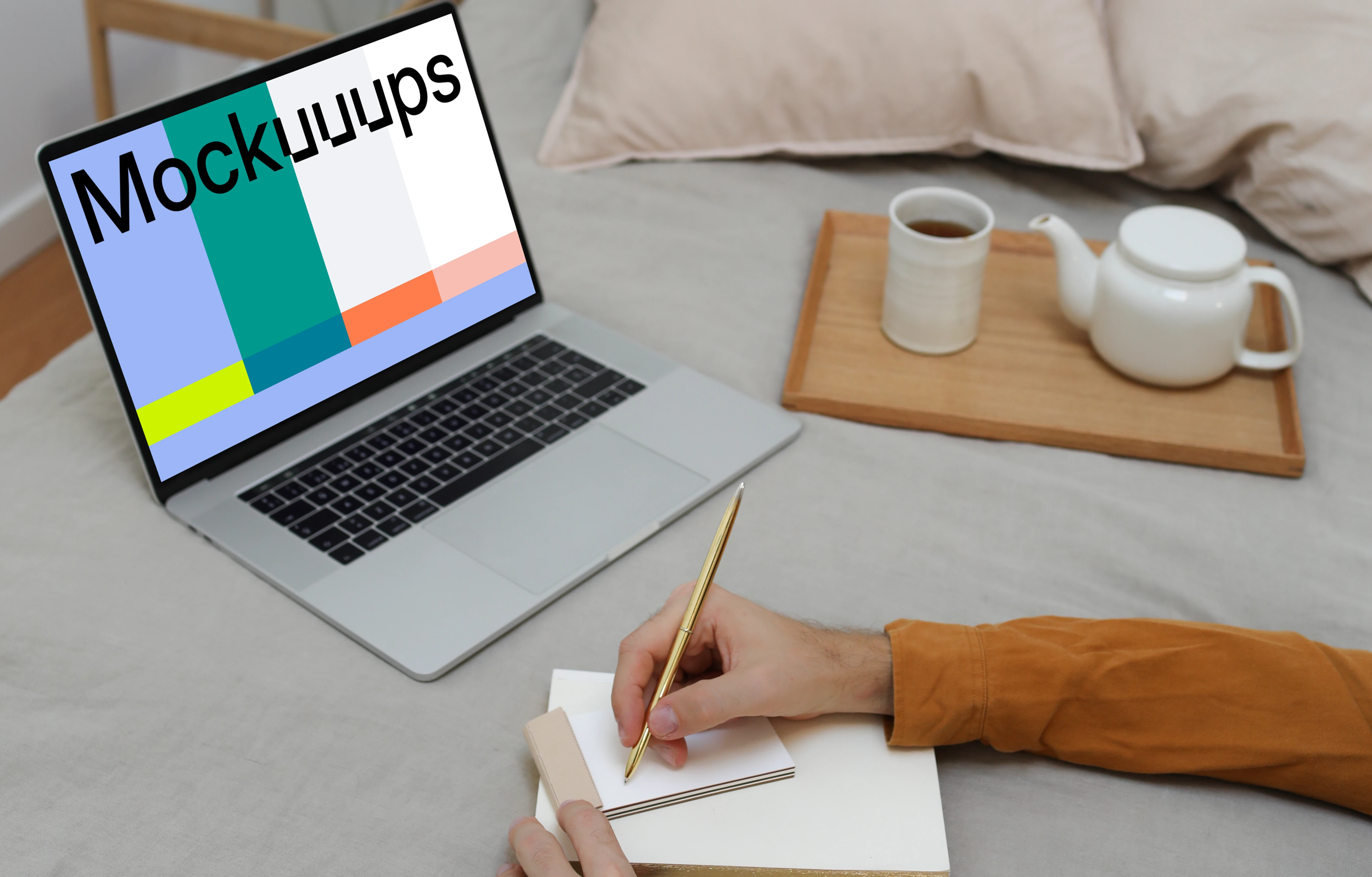 MacBook mockup on a bed with a user writing on a notebook