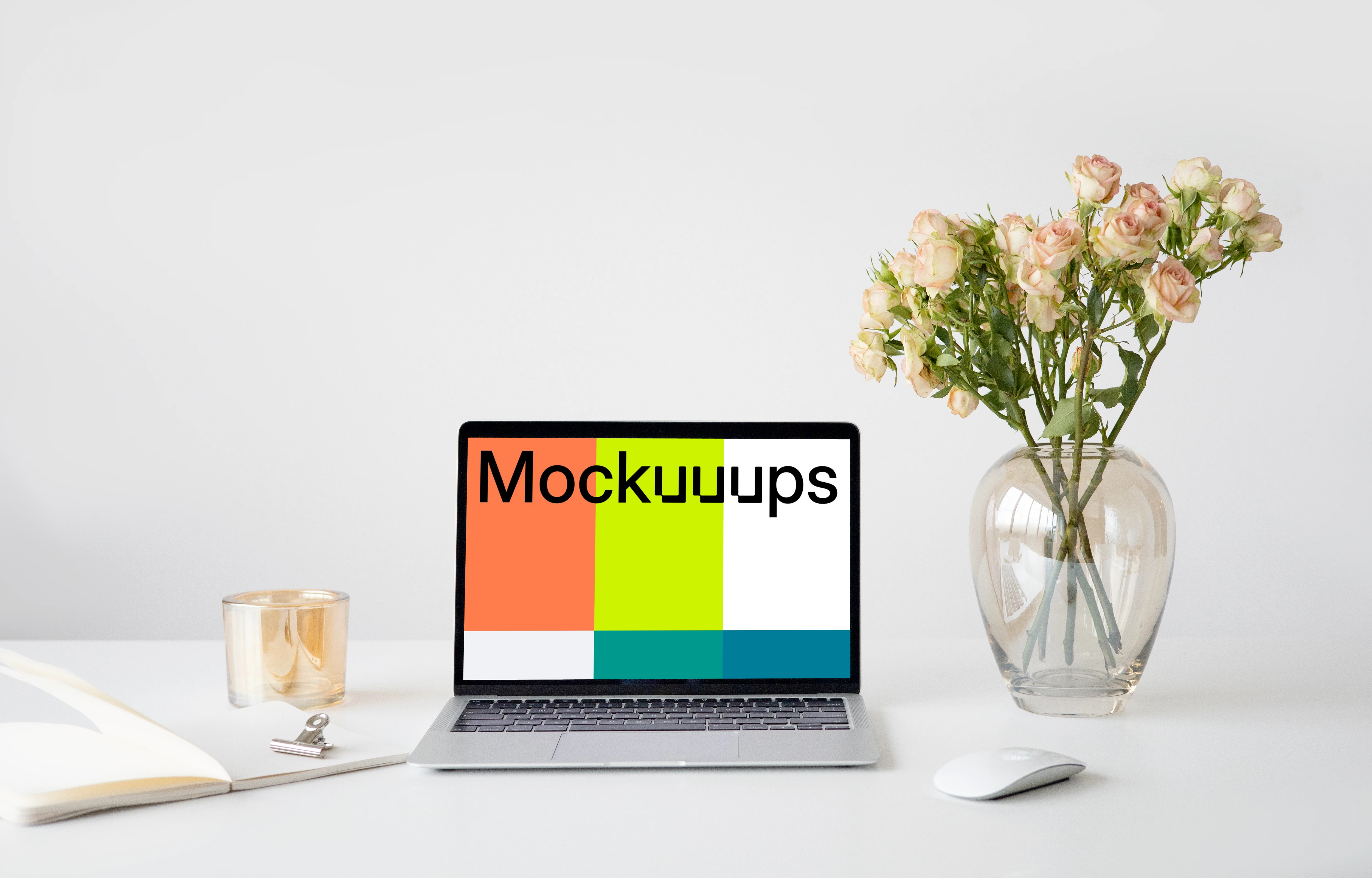 MacBook mockup on a white table with a wireless mouse and a vase of rose