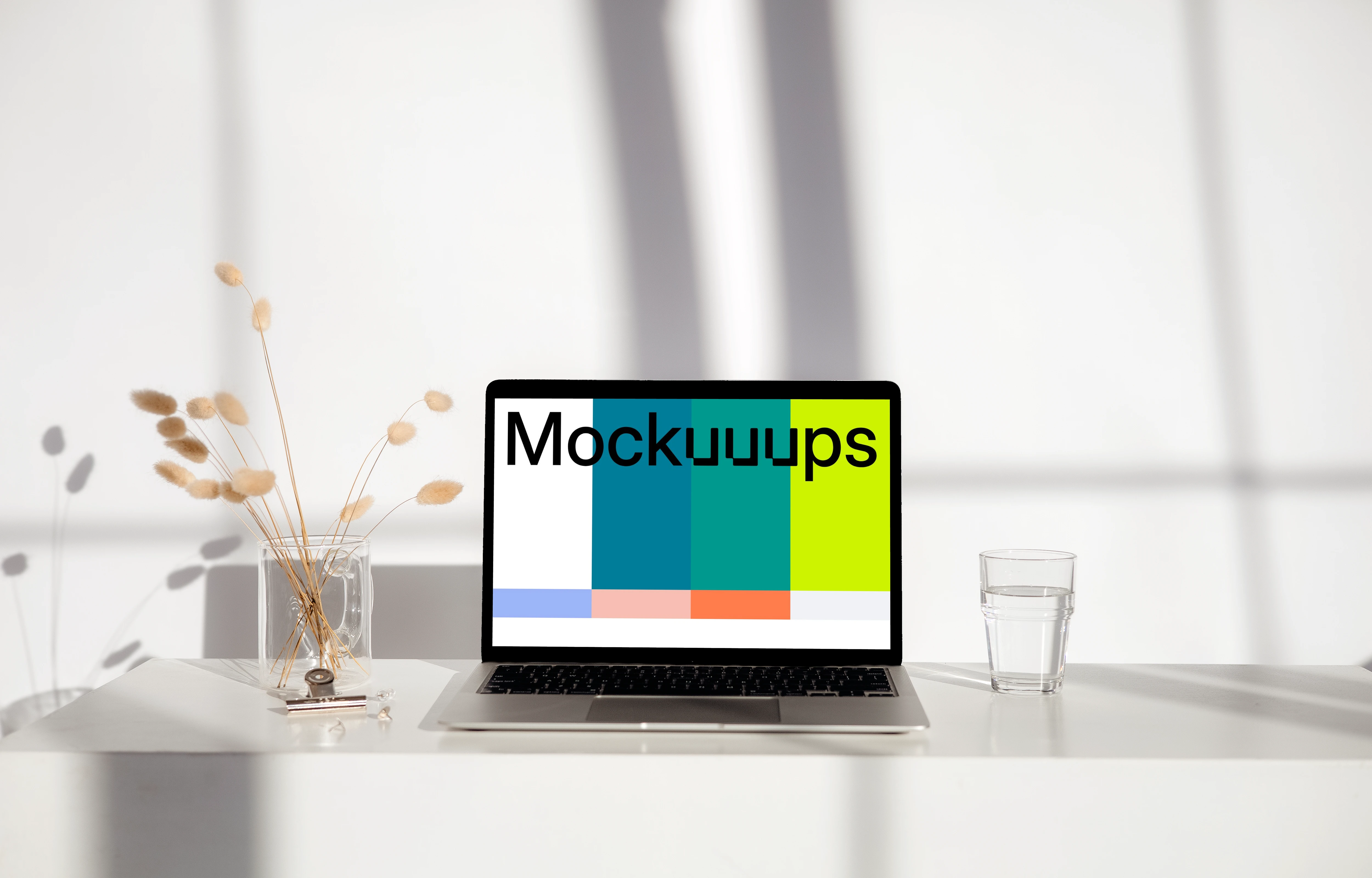MacBook mockup on a white table with glass of water next to it