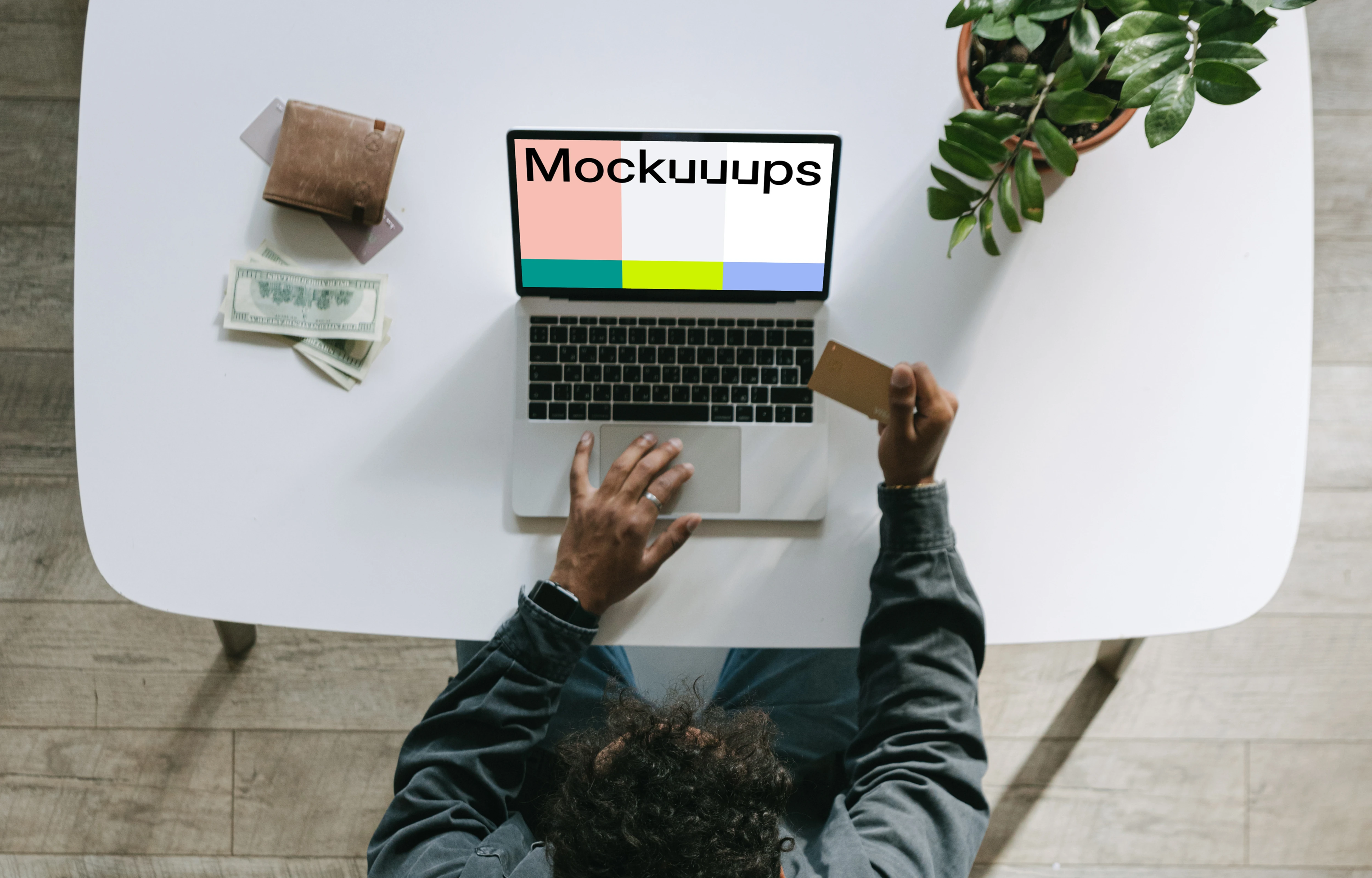 Mockup of man paying for an item on a grey MacBook beside a wallet.