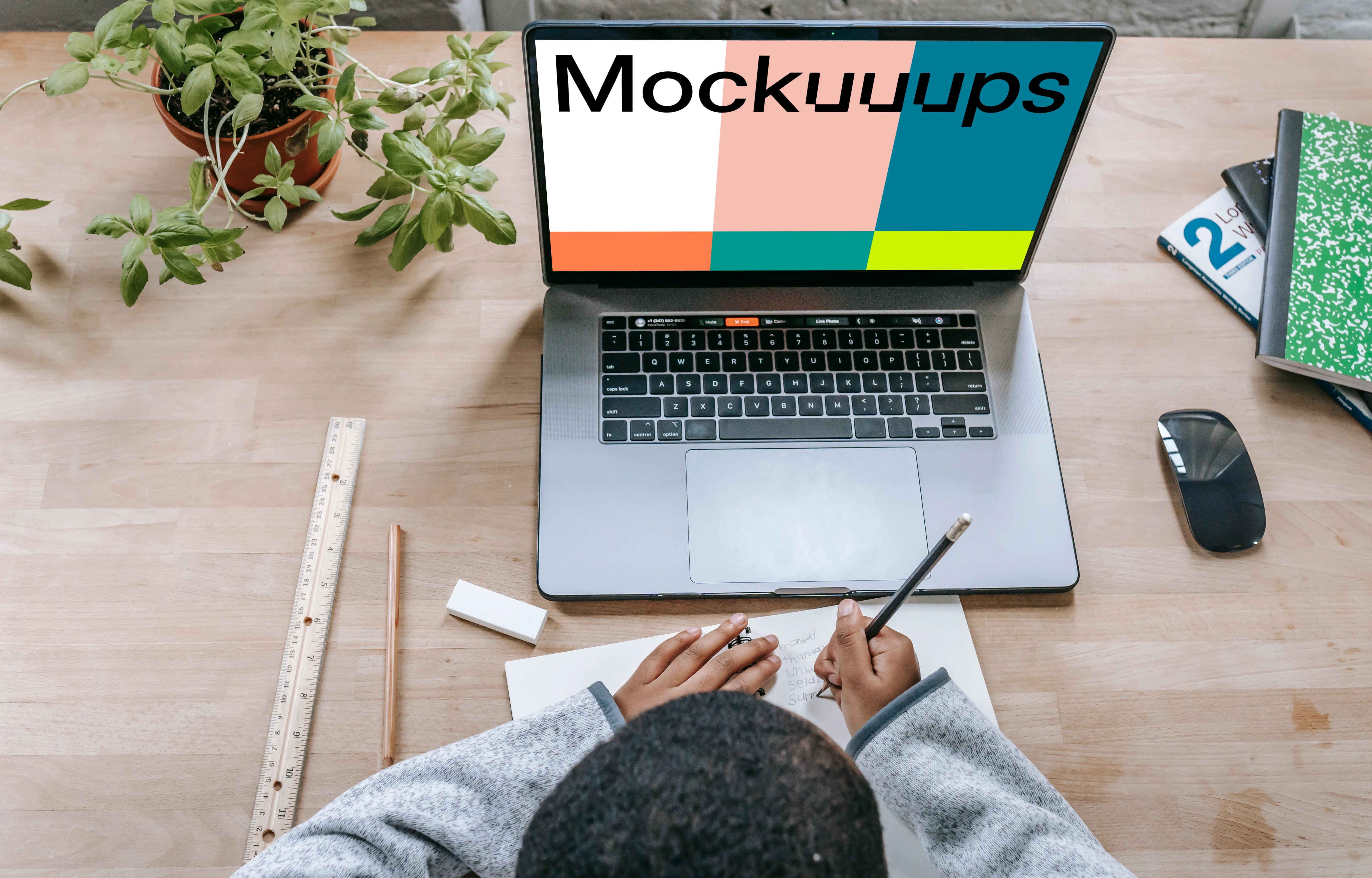 Young boy writing in a book with a MacBook Pro on the same table