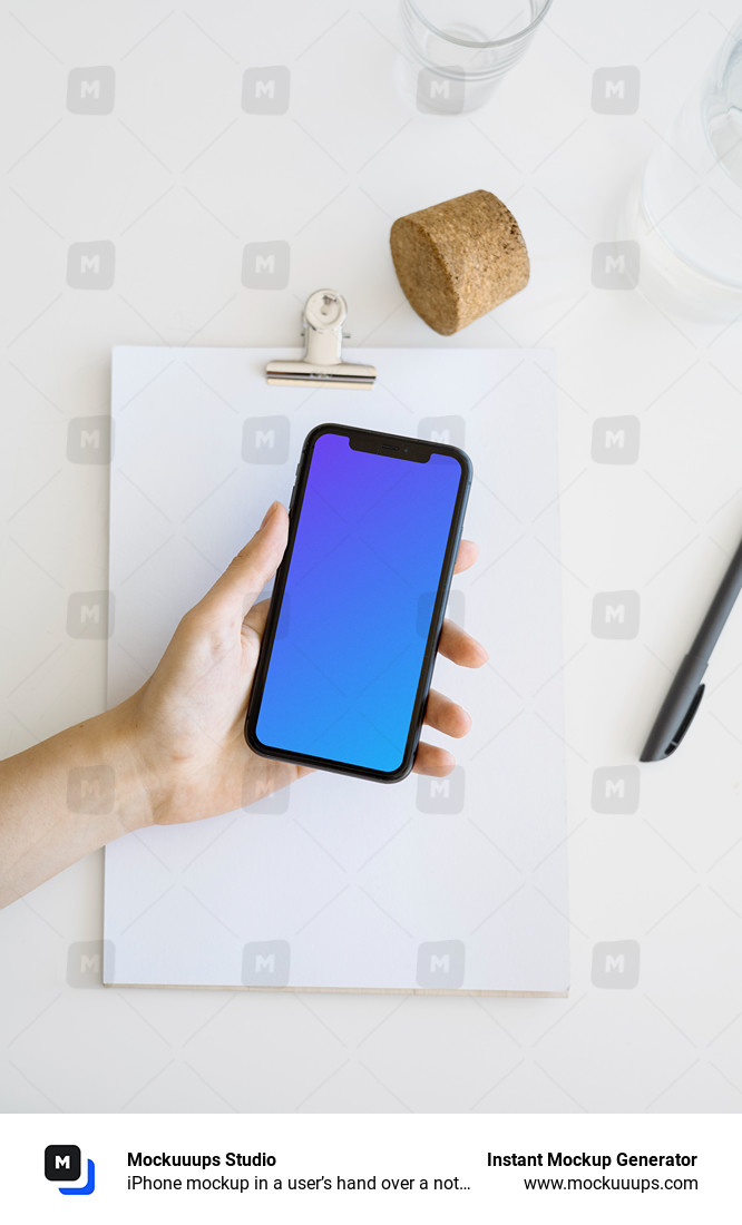 iPhone mockup in a user’s hand over a note pad and a cork