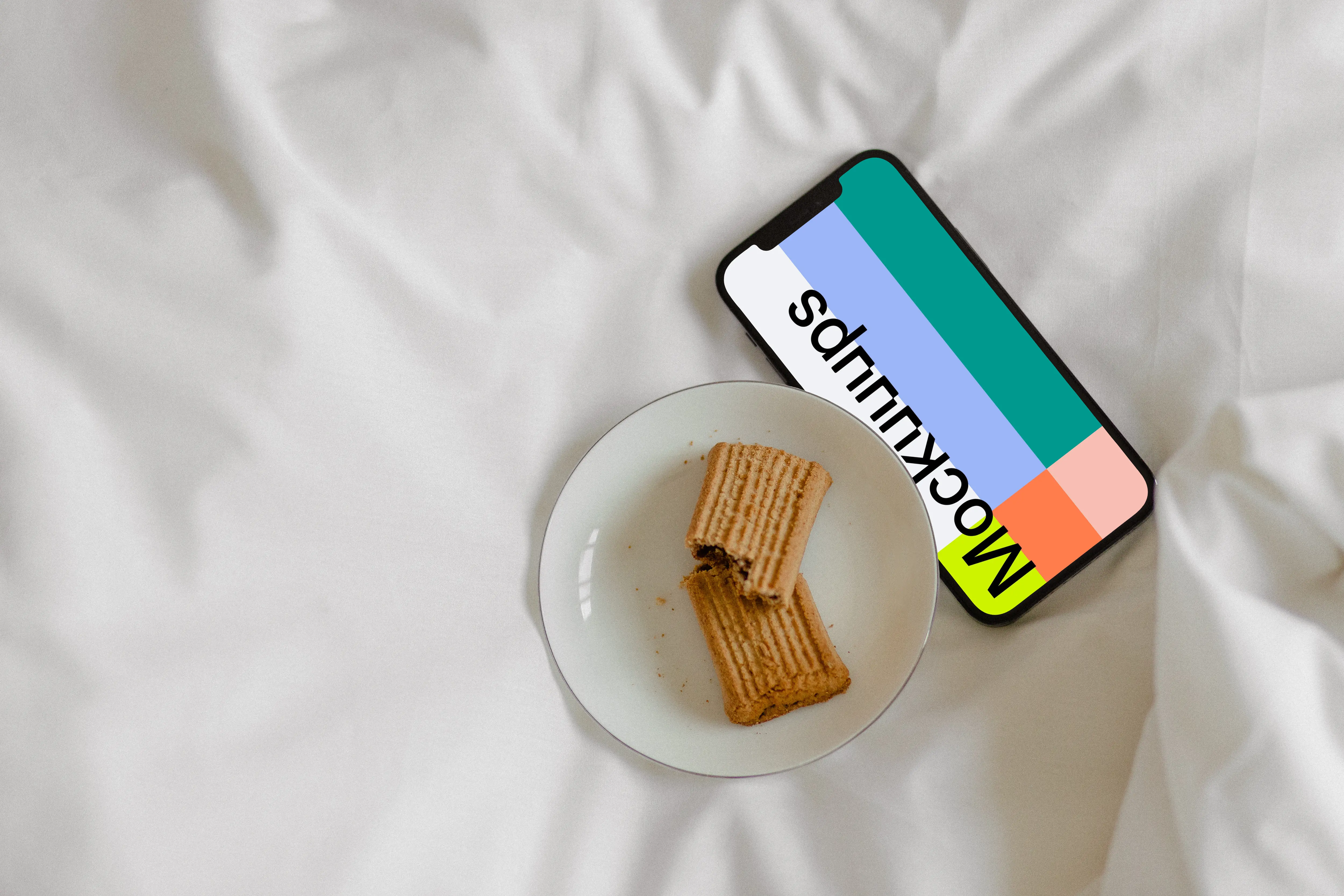 iPhone 12 Pro mockup on bed with a plate of biscuits