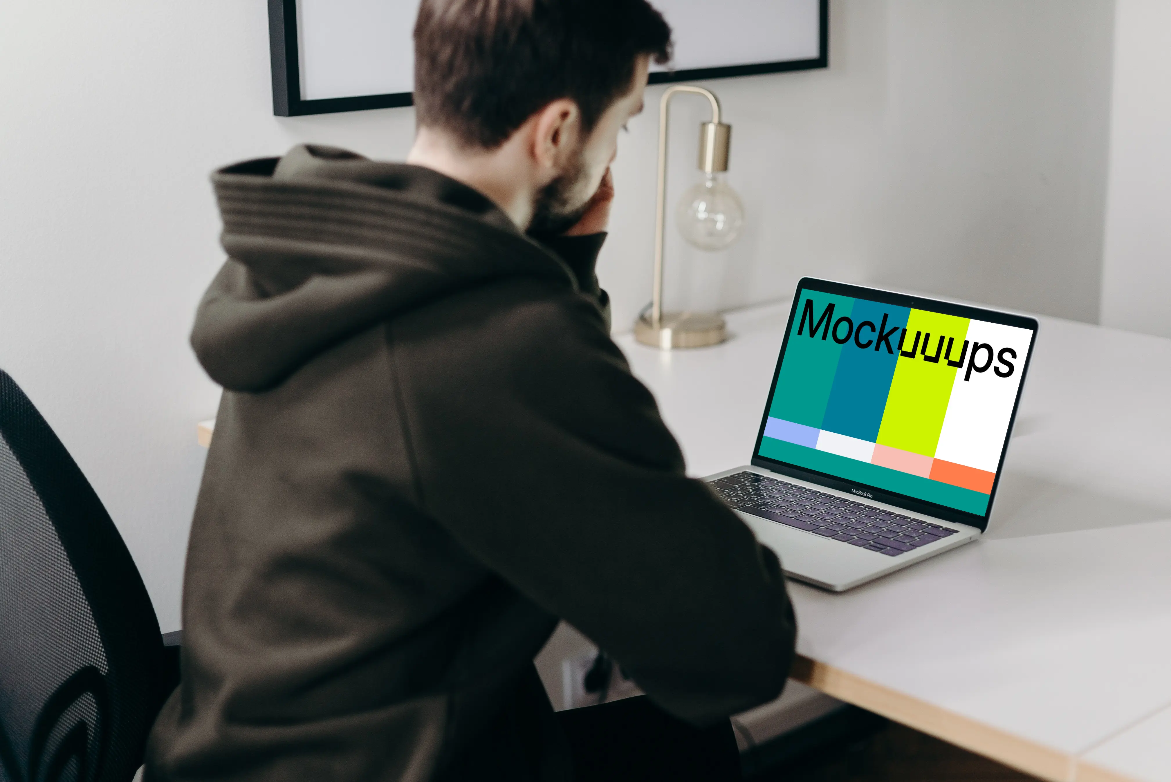 MacBook Pro mockup on a white table being used by a man in a black hoodie